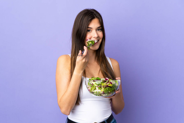 tiener Braziliaanse meisje met een salade over geïsoleerde paarse achtergrond - Foto, afbeelding
