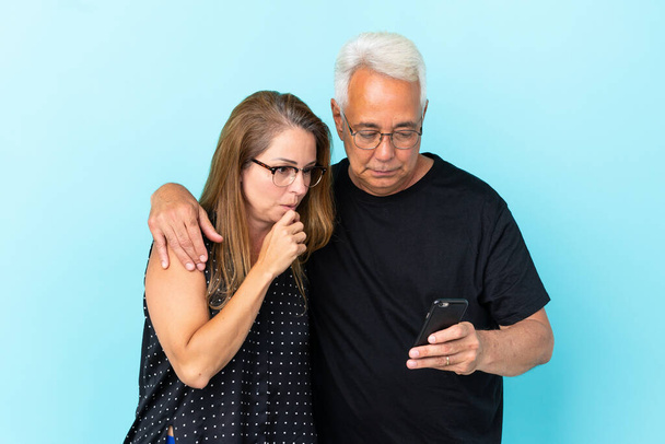Coppia di mezza età isolata su sfondo blu che legge un messaggio con il cellulare - Foto, immagini