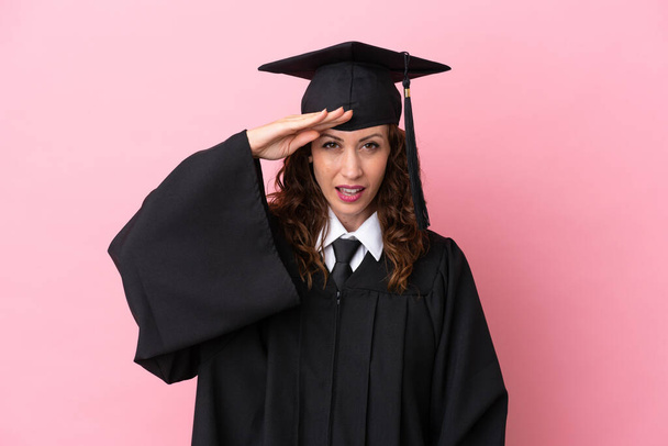 Молода випускниця університету ізольована на рожевому фоні, дивлячись далеко з рукою, щоб щось виглядати
 - Фото, зображення