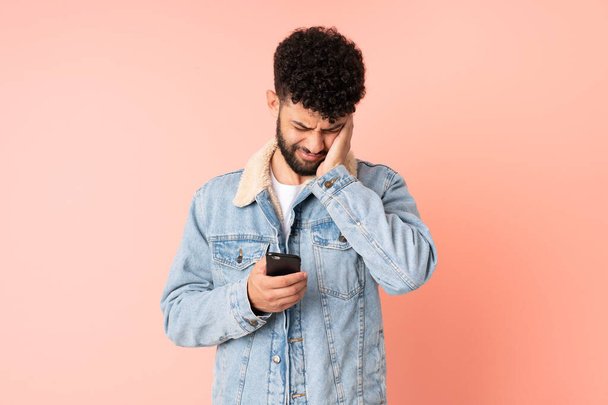 Joven hombre marroquí usando teléfono móvil aislado sobre fondo rosa frustrado y cubriendo oídos - Foto, Imagen