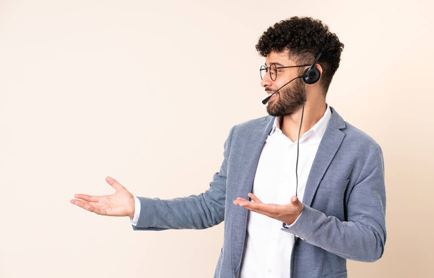 Telemarketer Moroccan man working with a headset isolated on beige background with surprise expression while looking side - Photo, Image