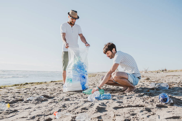 Egy csapat aktivista a parton gyűjti a műanyaghulladékot. Emberek takarítják a partot, táskákkal. A környezetvédelemmel és az óceánok szennyezésével kapcsolatos problémák fogalma - Fotó, kép
