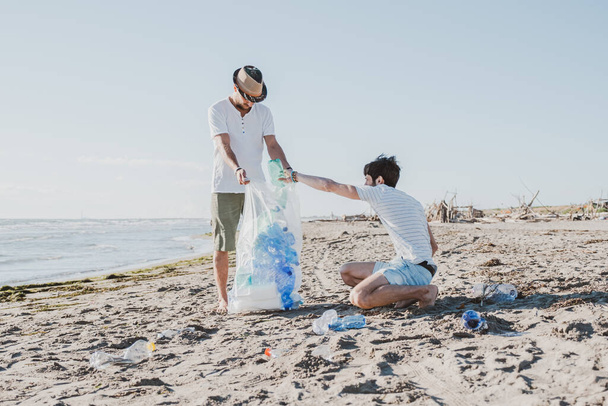 Grupa przyjaciół aktywistów zbierających odpady z tworzyw sztucznych na plaży. Ludzie sprzątający plażę z torbami. Koncepcja problemów związanych z ochroną środowiska i zanieczyszczeniem oceanów - Zdjęcie, obraz