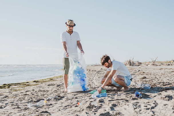 Grupo de amigos ativistas coletando resíduos de plástico na praia. Pessoas a limpar a praia, com sacos. Conceito de conservação ambiental e problemas de poluição dos oceanos - Foto, Imagem