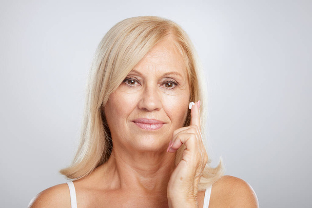 An attractive blond senior woman putting anti-age creme. Beauty photography - Zdjęcie, obraz