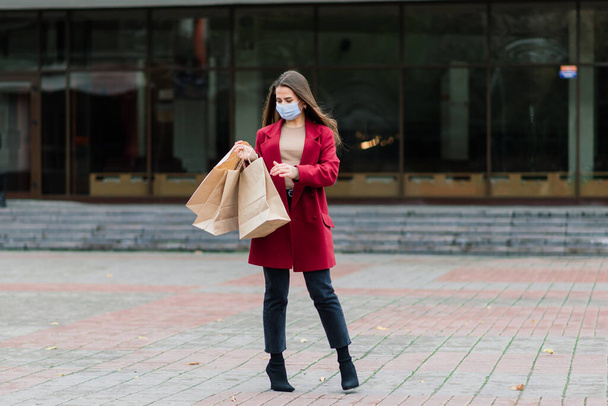 Portrait of a young fashion woman wearing protective mask with shopping bags on city street - Foto, afbeelding