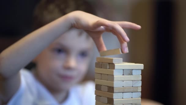 Мальчик играет в настольную игру с деревянной башней дома - Кадры, видео