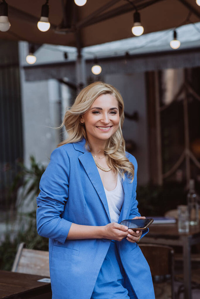Belle femme d'affaires en costume bleu avec un smartphone dans les mains, télétravail. Concentration sélective douce. - Photo, image