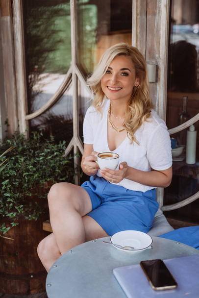 Красивая счастливая молодая женщина, деловая женщина, фрилансер, пользуется ноутбуком и выпивает чашку кофе в кафе во время обеда. Мягкая селективная фокусировка. - Фото, изображение