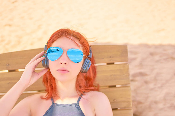 Όμορφη γυναίκα με γυαλιά ηλίου ακούγοντας μουσική στην παραλία. - Φωτογραφία, εικόνα