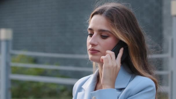 Close-up young business woman talking mobile phone in city street. Caucasian 30s girl answering call outdoors. Millennial client lady female serious student calling with smartphone cellphone outside - Footage, Video