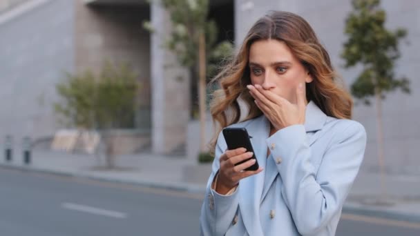 Kavkazské obchodní žena venku držet mobilní telefon číst nepříjemné sms hrozné zprávy pocit rozhořčení zakrývá ústa šokovaný obličej. Špatné upozornění z bankovního zablokovaného účtu zlomený úžas smartphone - Záběry, video
