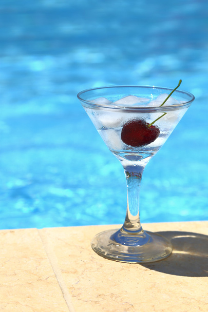koude cocktail met ijsblokjes en cherry door aan het zwembad - Foto, afbeelding