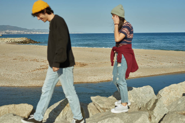Two engaged young people walking on rocks next to a beach - Fotografie, Obrázek