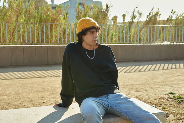 Cute young caucasian man looking thoughtful while sitting alone on a bench outdoors during the day - 写真・画像