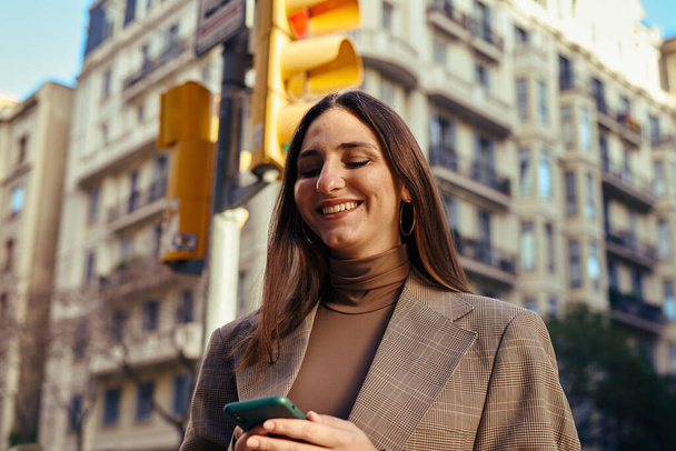 Elated lady in the street smiling while texting with a building and traffic light in the background - Photo, image