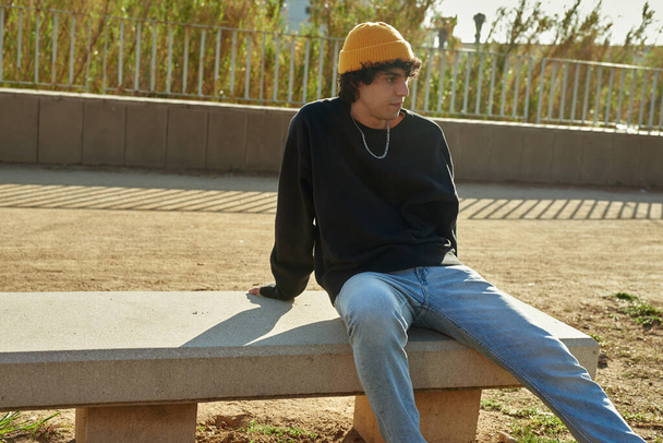 Handsome young caucasian man looking thoughtful while sitting alone on a bench outdoors during the day - 写真・画像