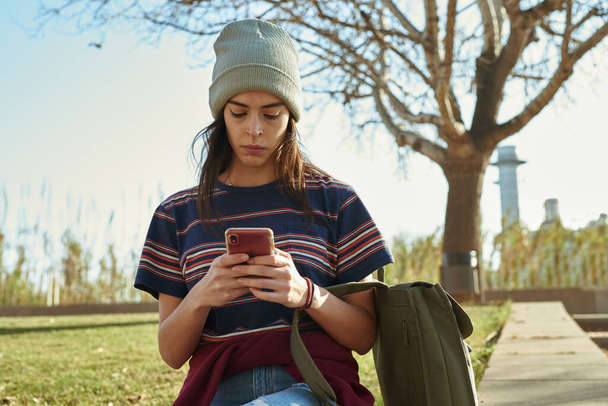 Attraente ragazza caucasica utilizzando un cellulare mentre seduto da solo all'aperto durante il giorno - Foto, immagini