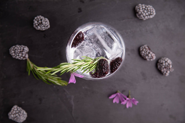A cup of gin and tonic with blackberries, a sprig of rosemary and a flower of ornament - 写真・画像