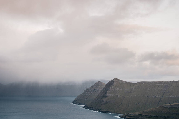 Faroe cliffs in mist. Morning Scandinavian landscape with mountains and fog over the fjord. Nordic landscape - Фото, зображення
