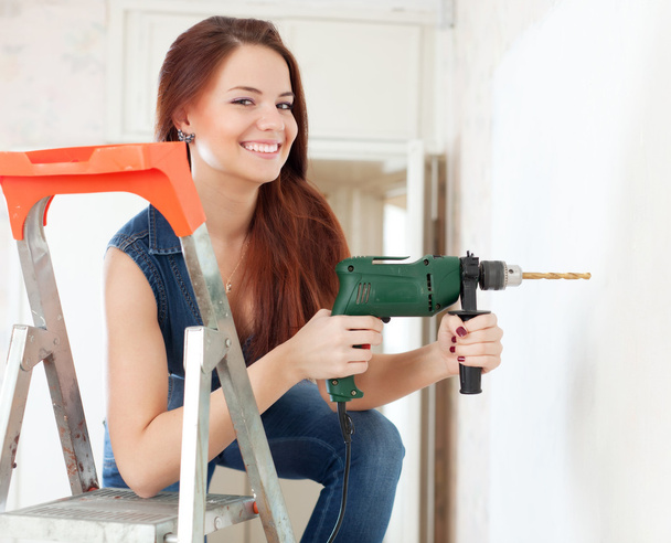 Happy woman drills hole in the wall   - Zdjęcie, obraz