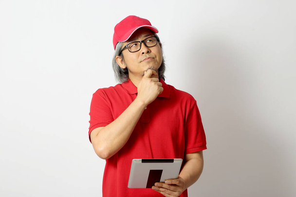 Ο Ασιάτης άνδρας ντυμένος κόκκινο πόλο πουκάμισο με κόκκινο καπάκι στέκεται στο λευκό φόντο. - Φωτογραφία, εικόνα