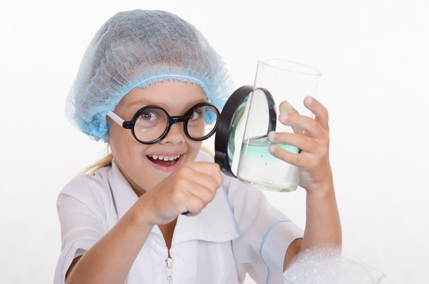 κορίτσι χημικός εξετάζει φιάλη κάτω από έναν μεγεθυντικό - Φωτογραφία, εικόνα