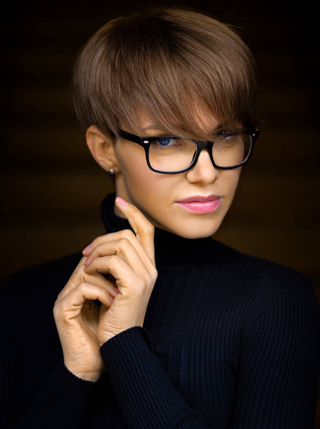 Portrait de mode d'une jeune femme élégante avec une coupe courte dans des lunettes sur un fond sombre. - Photo, image