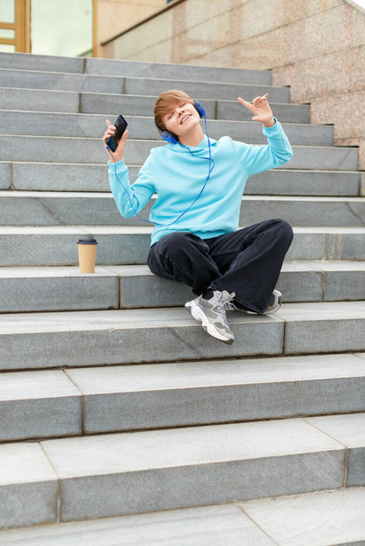 Függőleges fotó egy fiatal hipster nő ül a lépcsőn, és zenét hallgatni egy online okostelefon app és fejhallgató. Boldog és szabad.. - Fotó, kép