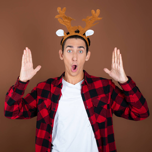 Christmas and New Year. A funny young guy enjoys the holidays. Brown background. - Photo, Image