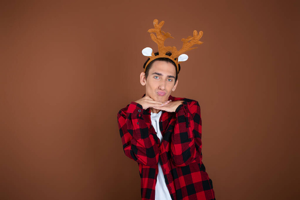 Christmas and New Year. A funny young guy enjoys the holidays. Brown background. - Photo, Image
