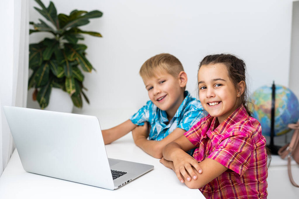 かわいい子供たちは教育、オンライン研究、家庭学習のためのラップトップを使用し、男の子と女の子は距離学習で宿題を持っています。家庭教育のライフスタイルコンセプト. - 写真・画像