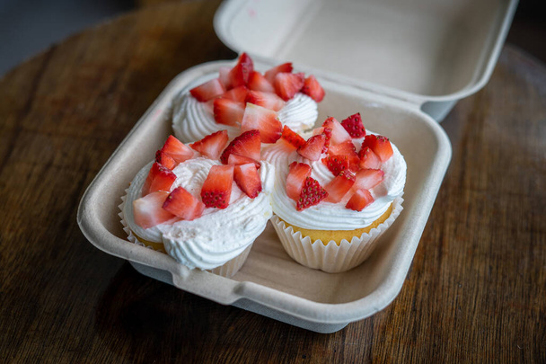 Homemade buttercream cupcakes with fresh strawberries in a take away container on wooden table. - Fotografie, Obrázek