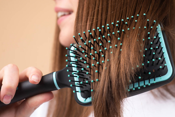 Close up smiling woman brushing hair with comb. Beautiful girl with long hair hairbrush. - Fotografie, Obrázek