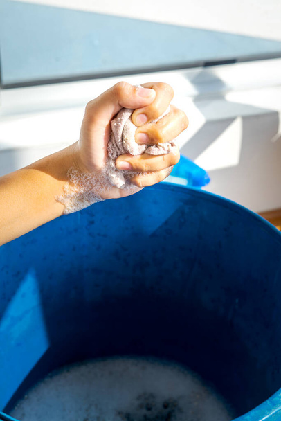 Stracci di mungitura a mano con bolle di sapone e secchio blu. Concetto di pulizia domestica durante la pandemia della congrega 19. - Foto, immagini