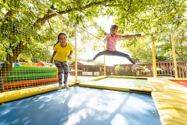 Pienet nätit tytöt pitävät hauskaa ulkona. Hyppääminen trampoliinilla lasten vyöhykkeellä. Huvipuisto
 - Valokuva, kuva