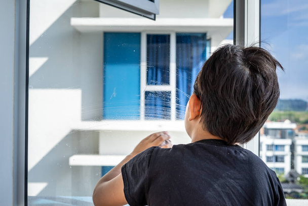 O conceito de limpeza de apartamentos em casa. Um rapaz na janela e limpa com um pano. vista por trás. - Foto, Imagem