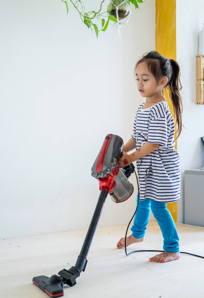 Cute little girl czyszczenia drewnianej podłogi z odkurzaczem - Zdjęcie, obraz