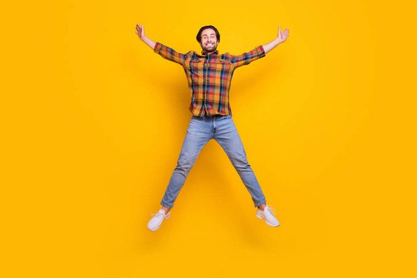 Full size photo of sweet brunet millennial guy jump wear shirt jeans sneakers isolated on yellow background - Fotoğraf, Görsel