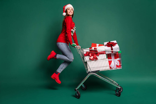 Full body profile photo of sweet young lady with trolley jump wear sweater cap jeans boots isolated on green background - Φωτογραφία, εικόνα