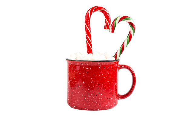 Κόκκινη κούπα με ζαχαρωτά και καραμέλα ζαχαροκάλαμου σε σχήμα καρδιάς σε λευκό φόντο απομονωμένη. Χριστούγεννα, Πρωτοχρονιά, εορταστική διάθεση. - Φωτογραφία, εικόνα