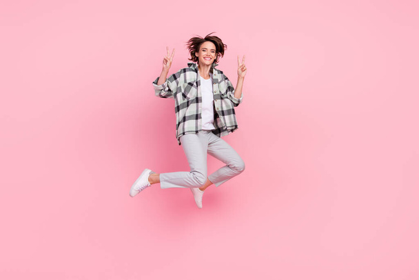 Full body photo of young woman happy positive smile show peace cool v-sign jump isolated over pink color background - 写真・画像