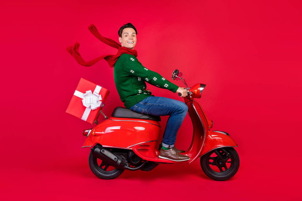 Full length body size photo smiling guy sitting on bike in scarf driving scooter isolated vibrant red color background - Foto, Bild