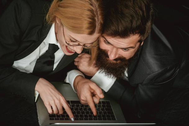 Young business woman and handsome businessman in suits are using a laptop in dark room. Portrait of a amazed business couple looking at laptop computer isolated on black. - Φωτογραφία, εικόνα