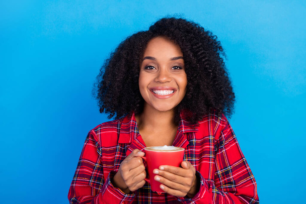 Photo of optimistic wavy hairstyle young lady hold cup wear red checkered pajama isolated on blue color background - Фото, зображення