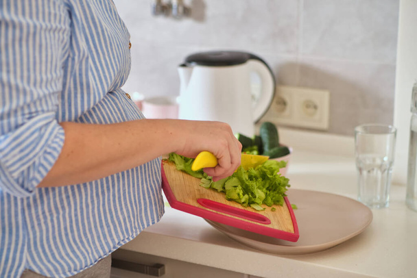 Close up pregnant woman with knife on kitchen cuts salad - Zdjęcie, obraz