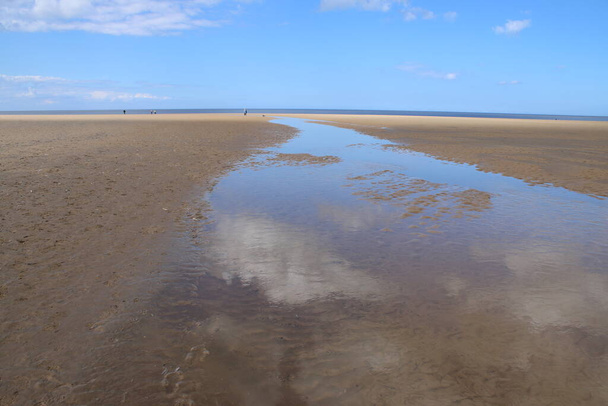 Landschap van prachtige zandstrand zonder mensen en zand uitgerekt tot horizon met witte gezwollen wolken weerspiegeld in het water zwembaden in Holkham noord Norfolk East Anglia uk - Foto, afbeelding