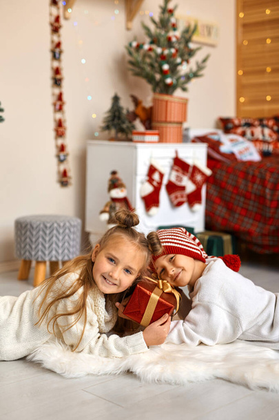 Neşeli küçük erkek ve kız kardeşler Noel için süslenmiş çocuk odasında yere yatar ve güzel bir hediye kutusunu bir arada tutarlar.. - Fotoğraf, Görsel