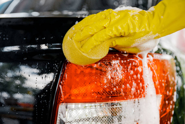 Una mano di donna con una spugna gialla per lavare, lavare un'auto. - Foto, immagini