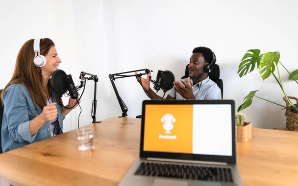 Des personnes multiraciales enregistrant un podcast à l'aide d'un microphone et d'un ordinateur portable depuis leur studio - Photo, image